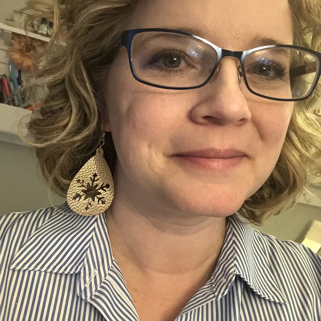 Chelly Ontis wearing handmade earrings with a floral design, smiling at the camera.