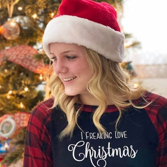Smiling girl looking away with shirt mockup, "I freaking love Christmas" SVG and Christmas tree in the background.