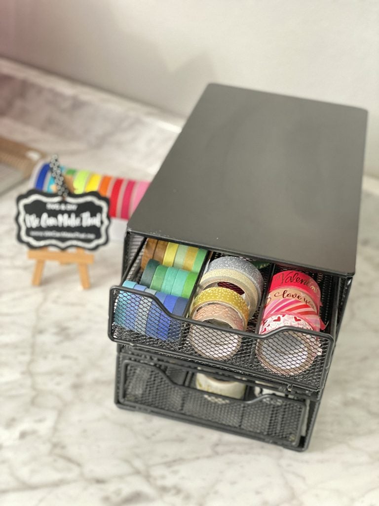 A desktop organizer with rolls of washi tape. In the background, a colorful set of tapes is visible next to a small chalkboard sign that reads 'We Can Make That.'