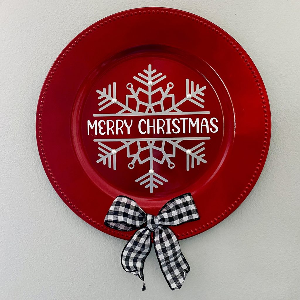 Red charger plate decor with Merry Christmas and snowflake SVG design with black and white checkered bow.