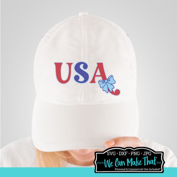 White baseball cap with the USA with Bow design applied on the front panel, modeled by a person looking down.