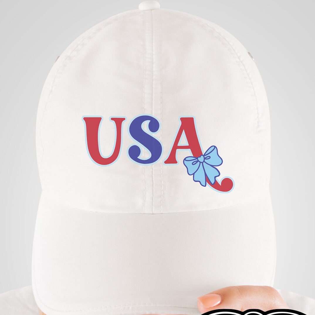 White baseball cap with the USA with Bow design applied on the front panel, modeled by a person looking down.