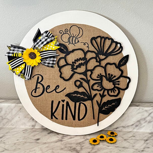 Circle wooden sign with a bee graphic and black wooden flowers.