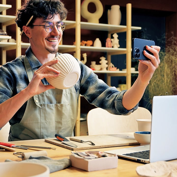 Craft business owner (male) taking picture of her pottery.