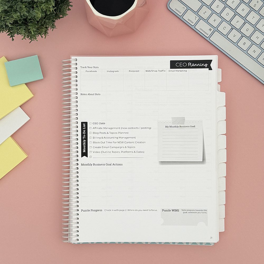 Small business planner open on pink desk.