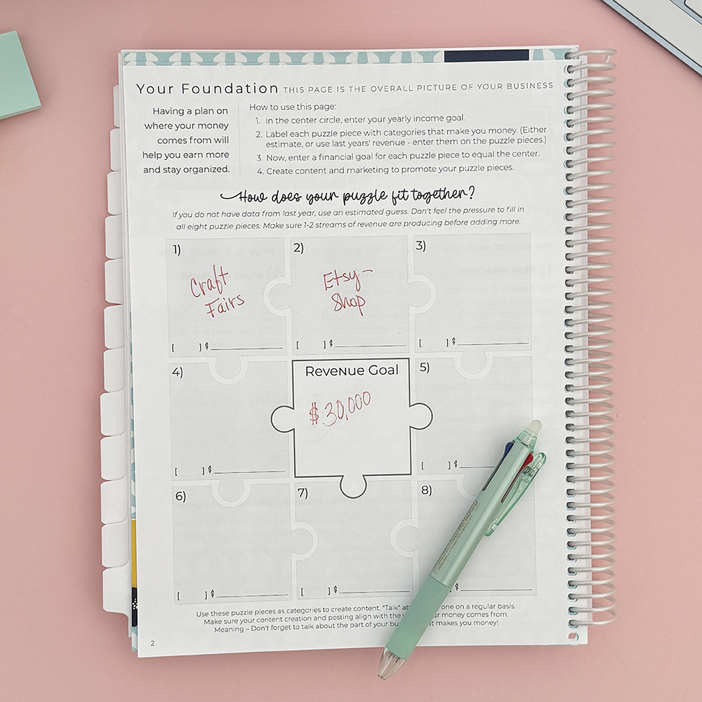 Small business planner open on pink desk.